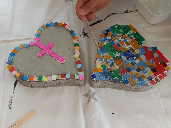 Zwei herzförmige Betonplatten werden mit bunten Mosaikfliesen verziert.
