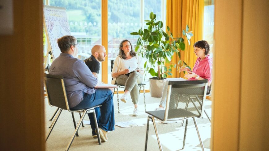 Ein Gruppenfoto aus unserer Akademie, das vier Erwachsene in einer Sitzrunde zeigt, die sich unterhalten.