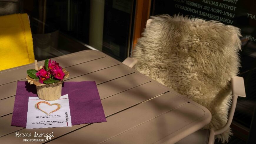 Ein Tisch mit Stuhl vor dem Hopsizhaus. Am Tisch steht ein Blumengesteck.