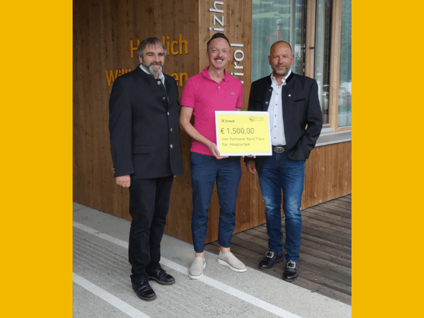 Hauptmann Horst Feichtner, Pflegedirektor Robert Profunser und Leutnant Martin Norz stehen vor dem Hospizhaus. Sie halten einen Scheck über 1.500 Euro in der Hand. Im Hintergrund ist die Holzwand des Hauses zu sehen.