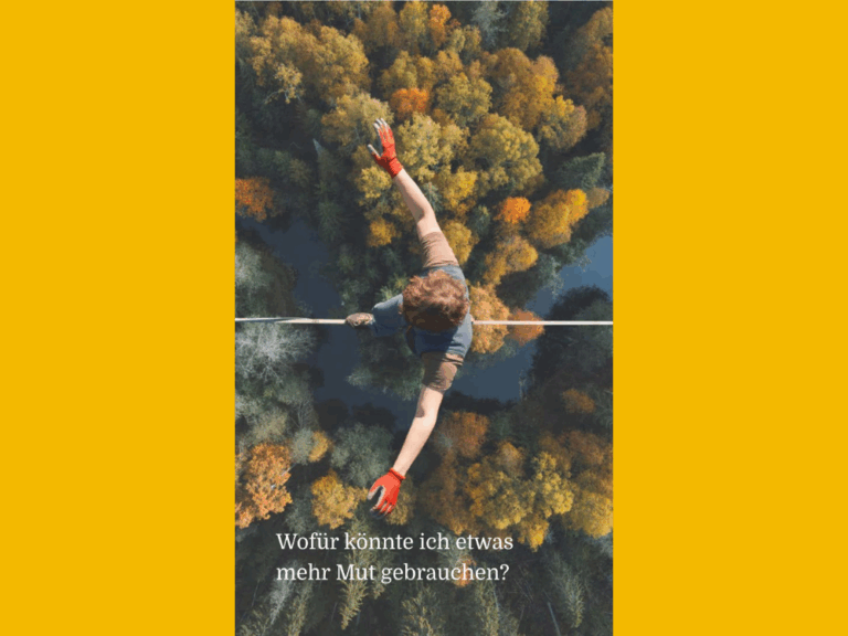 Eine Nahaufnahme aus der Vogelperspektive zeigt einen Menschen, der auf einem dünnen Seil über einem Wald mit einem Fluss balanciert. Die Person trägt orangefarbene Handschuhe und ein blaues T-Shirt. Unter dem Bild steht in weißer Schrift der Text: „Wofür könnte ich etwas mehr Mut gebrauchen?“ Das gesamte Bild ist von einem breiten, gelben Rand umgeben.